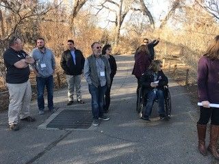 A group of people walking on a paved path in a park; one person in a wheelchair.