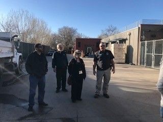 Four people standing outside on a sunny day near a truck and buildings.