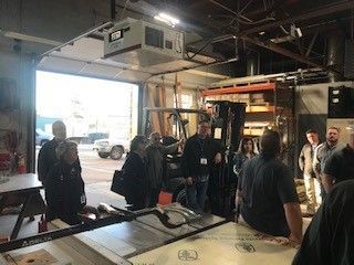 Group of people in a workshop with open door. A table saw is in the foreground.