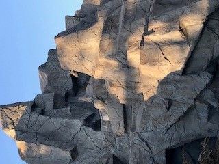 Gray, textured artificial rock climbing wall against a blue sky.