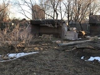 A dilapidated concrete structure sits in a field with dry grass and patches of snow. 