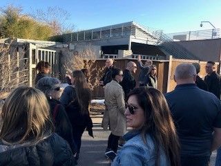 People gathered outside a building with security visible. Sunlight.