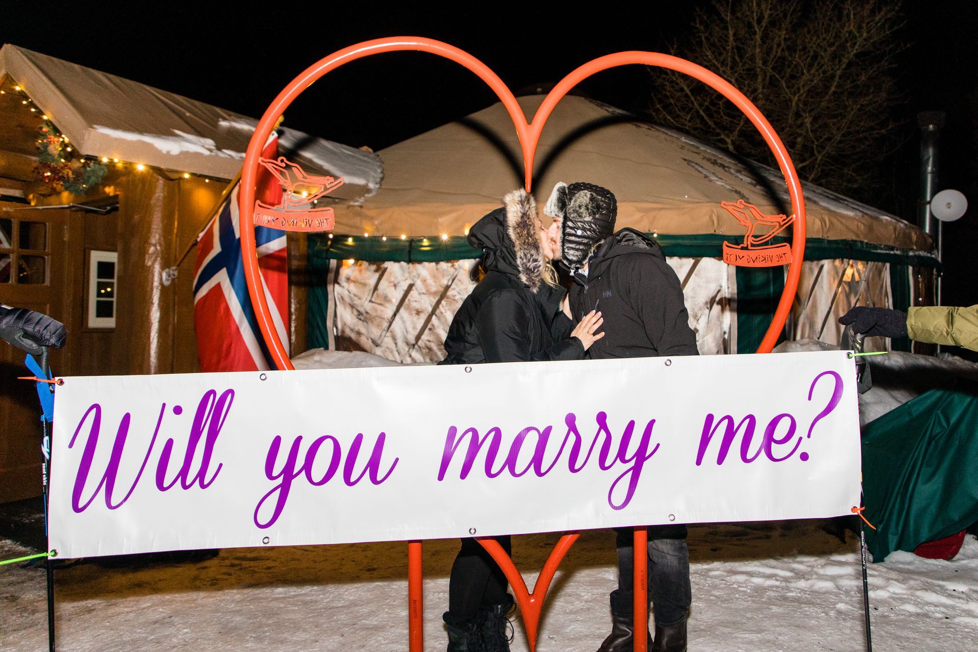 will you marry me banner on large metal heart with couple kissing