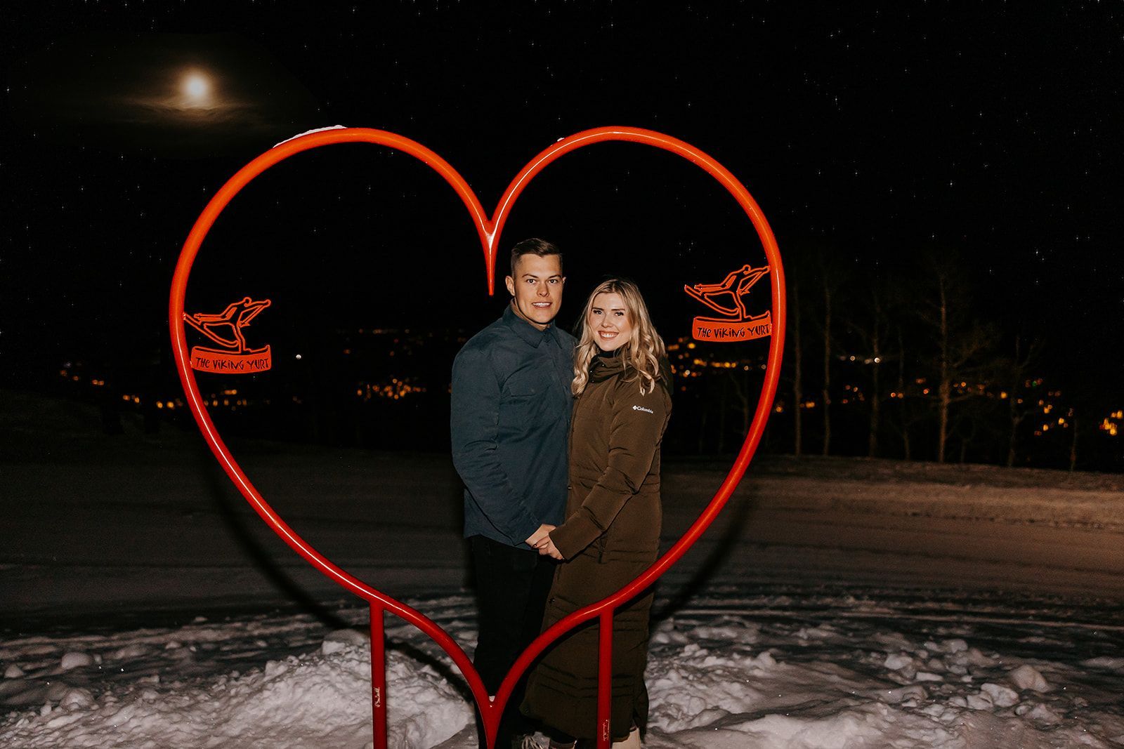 couple posing behind a large metal heart