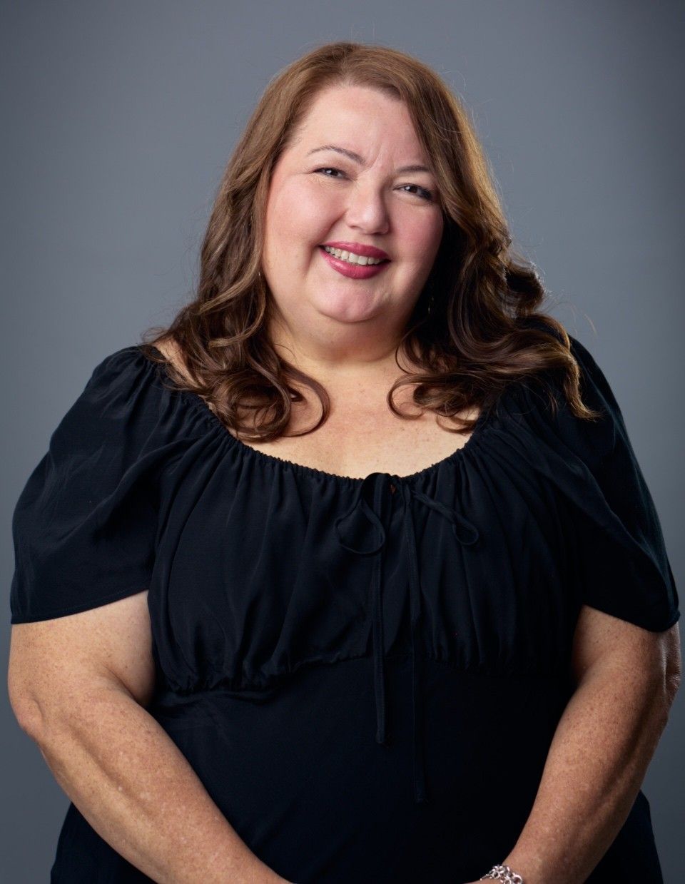 Woman with dark hair, wearing a blue top and black blazer, smiling at the camera.