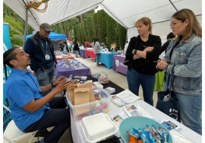 People at an outdoor event, gathered at a table with products and information.
