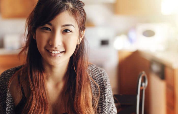 Young woman with long brown hair smiles warmly indoors.