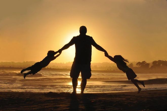 Father spinning two children on a beach at sunset.