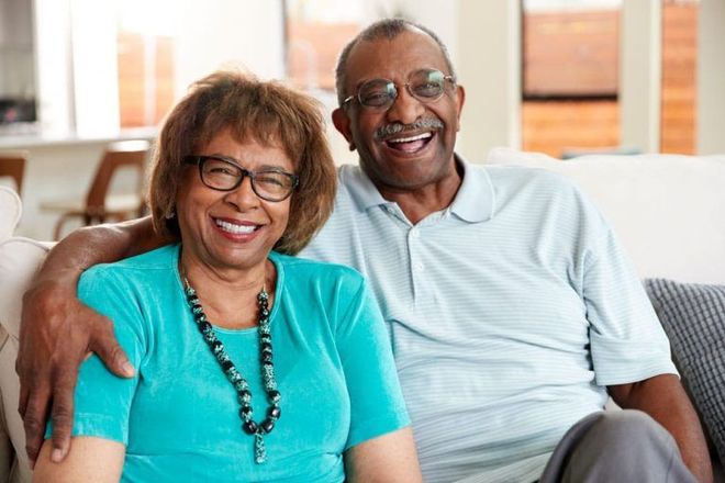 Smiling senior couple on a couch. Woman in turquoise shirt, man in polo. Indoor setting.