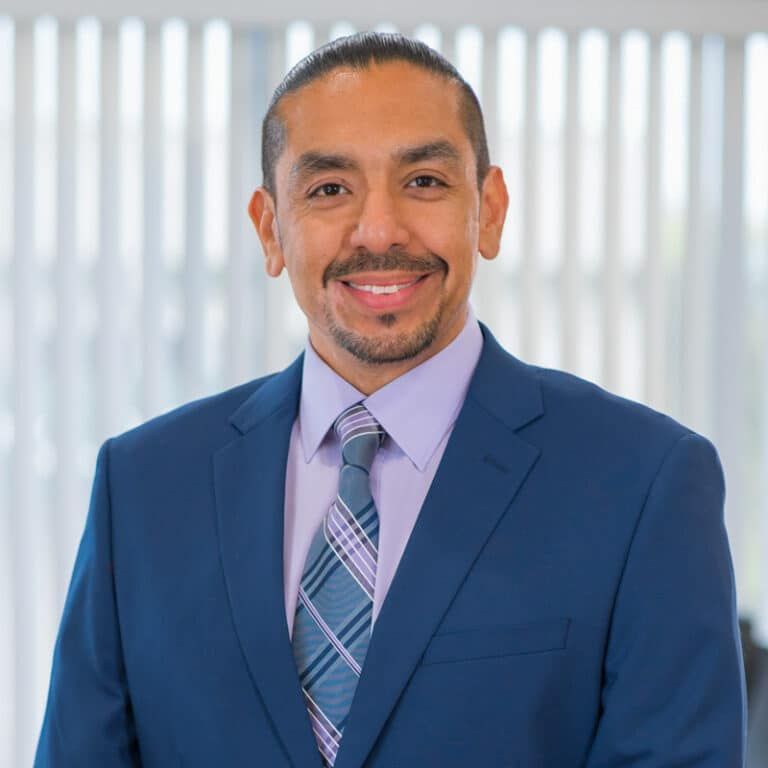Man in blue suit smiles at the camera; light-colored background.