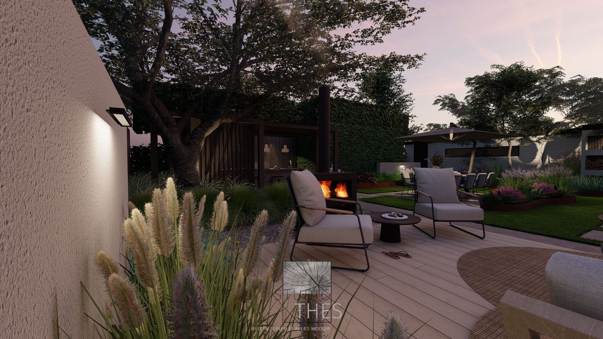 Een foto in de avond van een tuin met een vlonder en stoelen. Ervoor grassen en erachter een overkapping met buitenkeuken