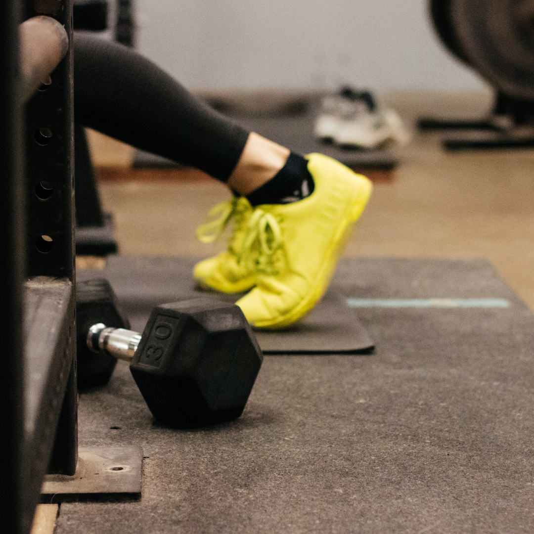 A person is sitting on a bench in a gym next to a dumbbell.