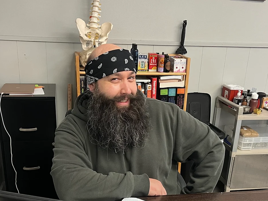 A man with a beard wearing a bandana is sitting at a desk.