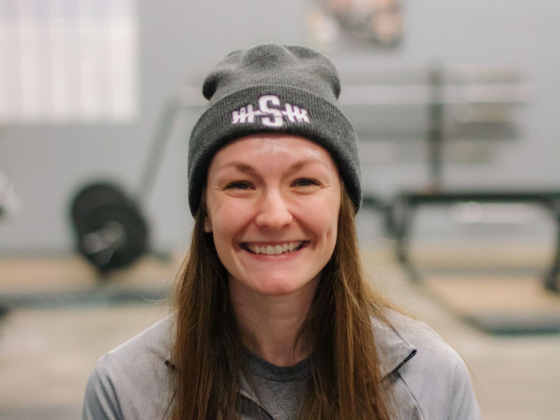 A woman wearing a beanie and smiling in a gym.