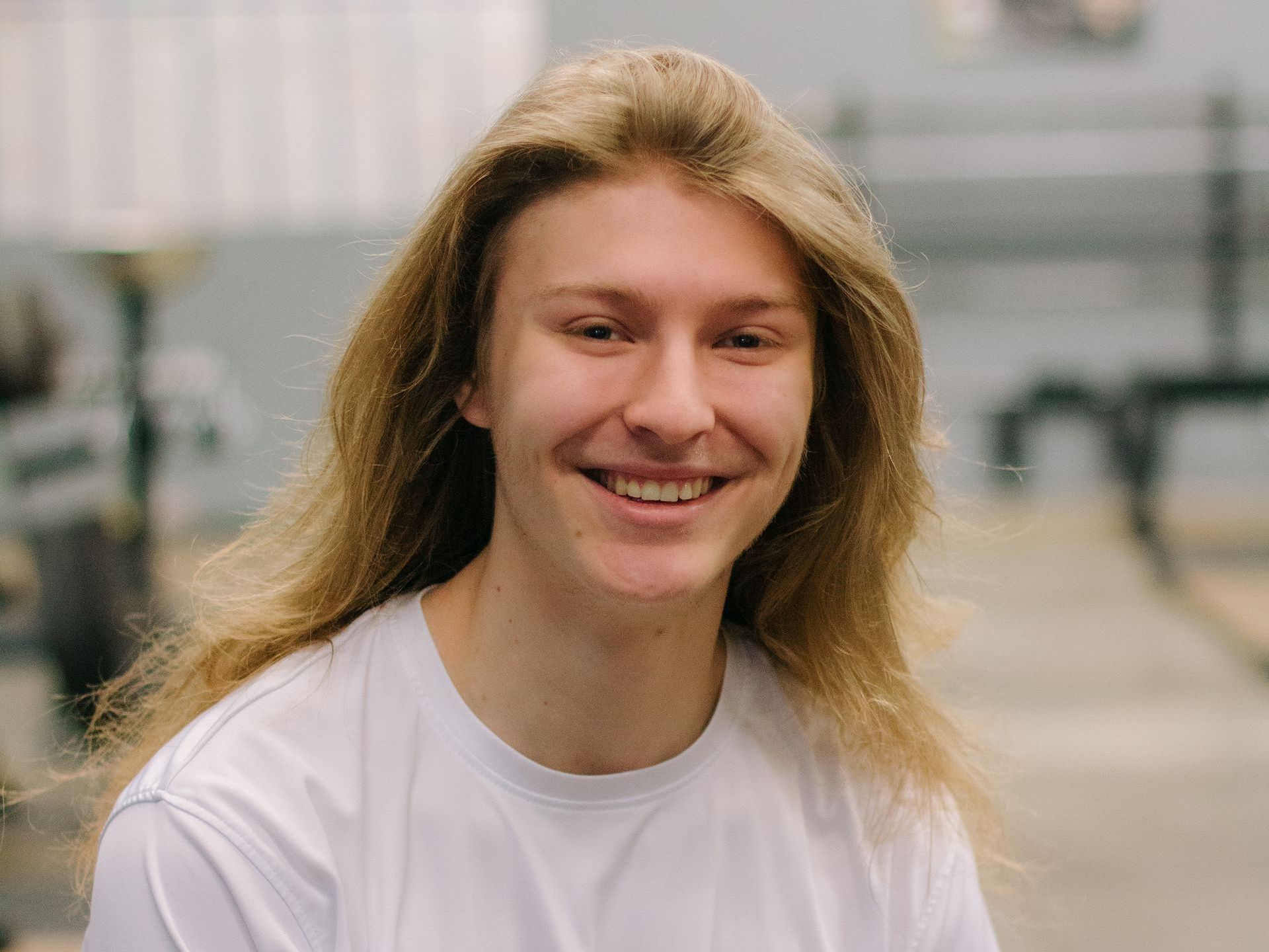 A young man with long blonde hair is smiling for the camera.