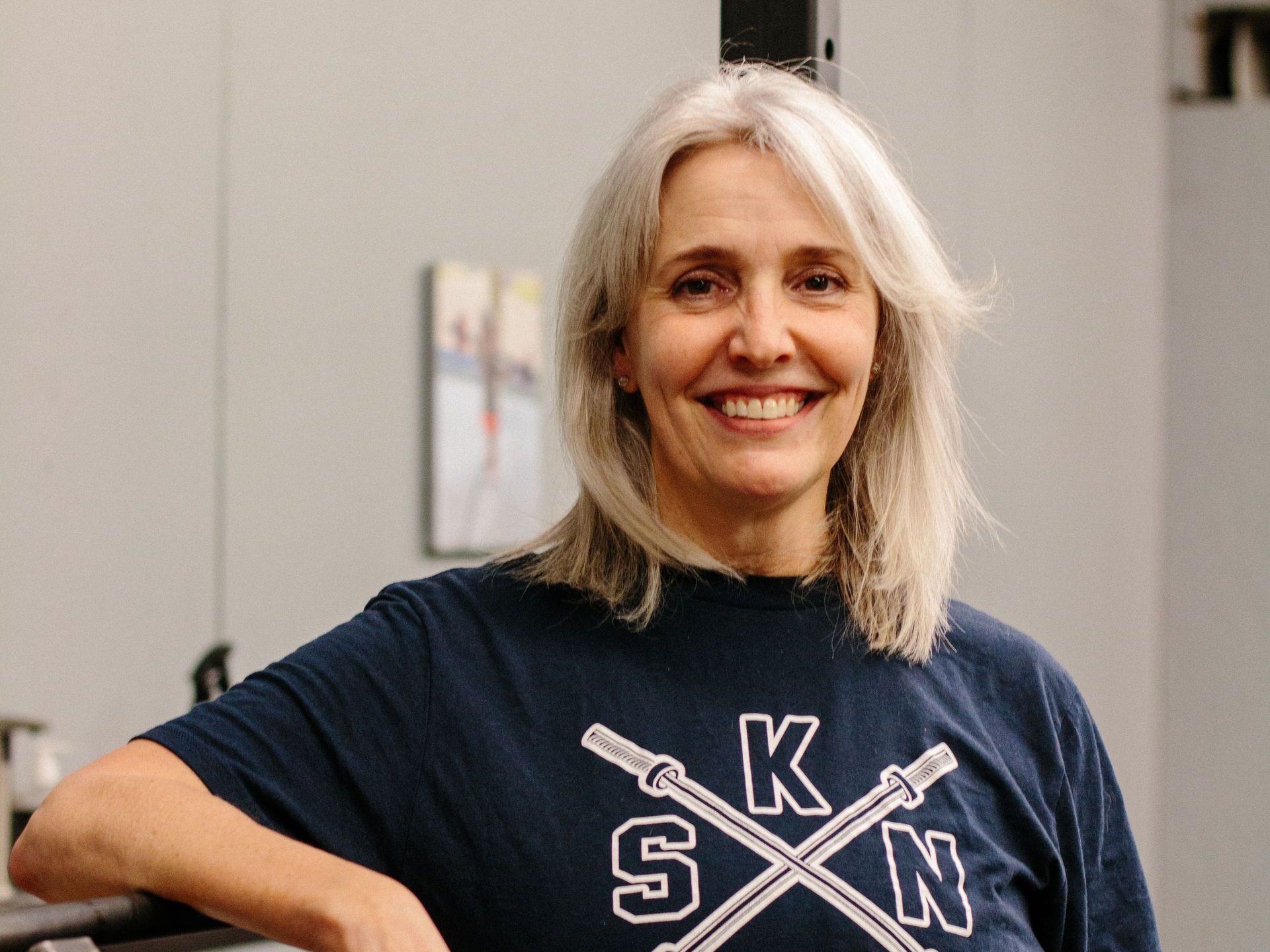 A woman wearing a blue shirt with the letter k on it is smiling.