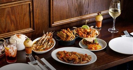 A table set with a variety of gourmet dishes, including shrimp, rice, appetizers, and a glass of wine.