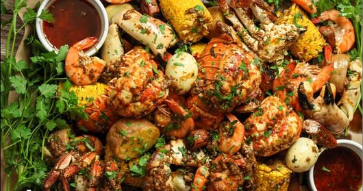A seafood boil platter with crab, lobster, shrimp, potatoes, and corn on the cob, garnished with parsley and dipping sauce.