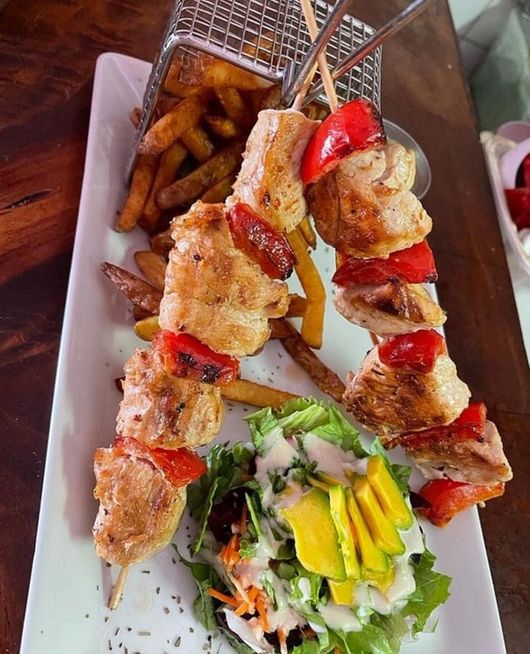 Two skewers of grilled chicken and red peppers served with a wire basket of fries and a side salad with avocado.