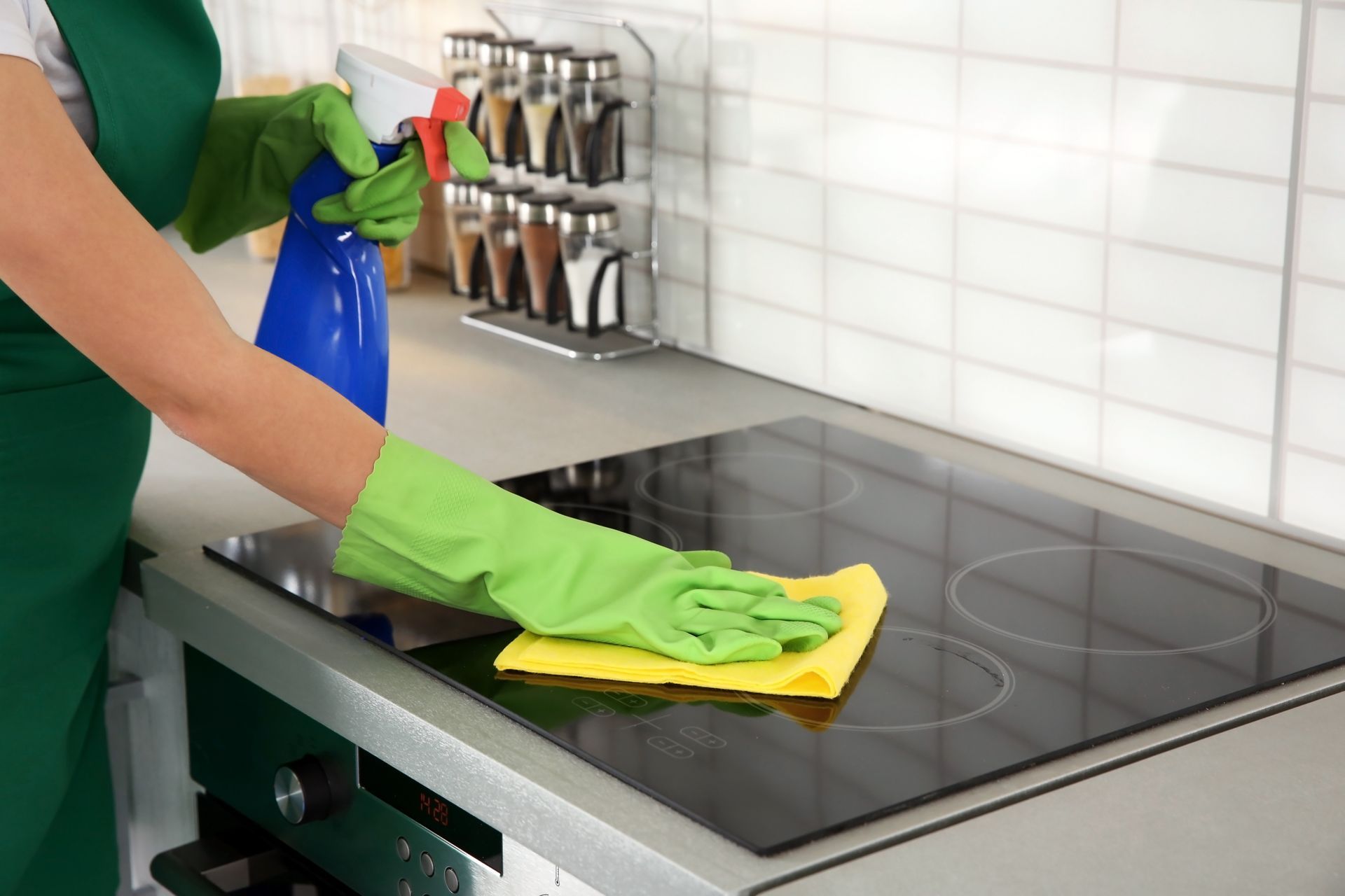 A woman is cleaning a stove top with a cloth and spray bottle.