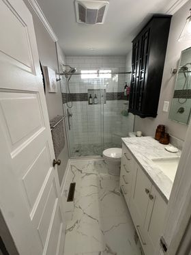 White bathroom with marble-look tiles, a vanity, toilet, and shower/tub combo. A decorative brown tile border accents the walls.