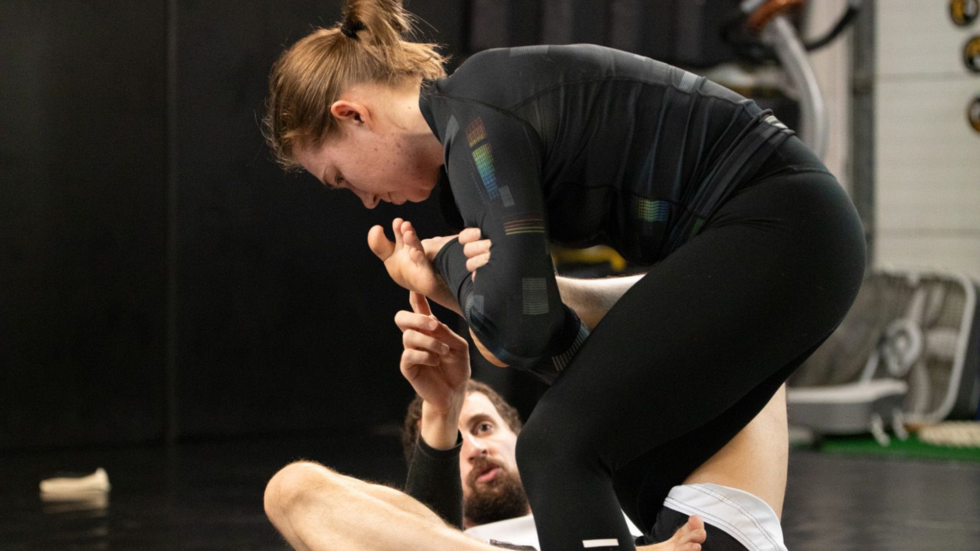 Woman practicing martial arts, gripping arm of person on the ground, in gym.