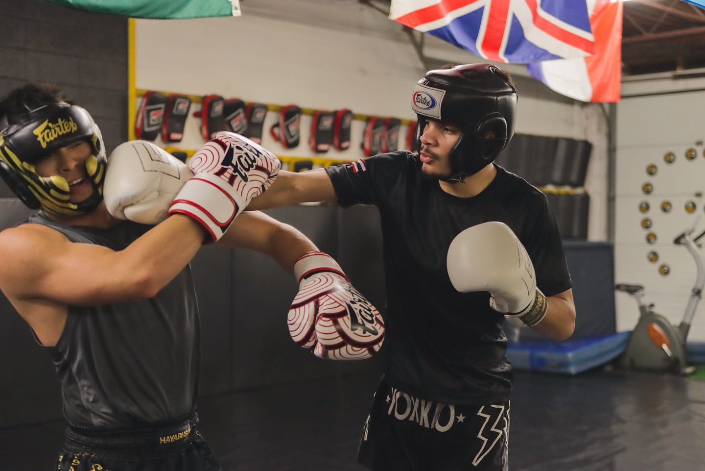 Two men are boxing in a gym with flags in the background