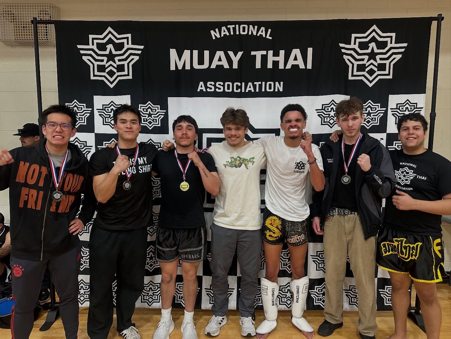 A group of young men are posing for a picture in front of a national muay thai association banner.