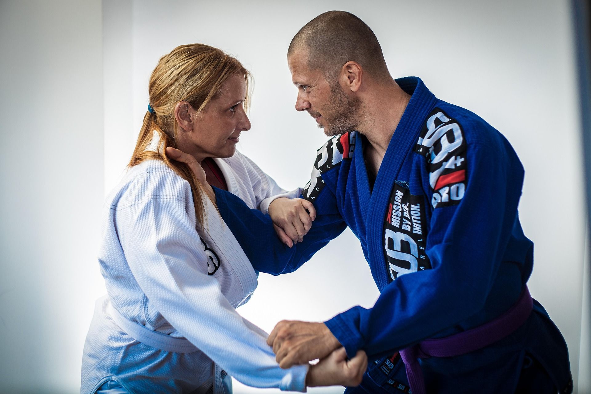 Two people in martial arts uniforms practice a grappling technique.