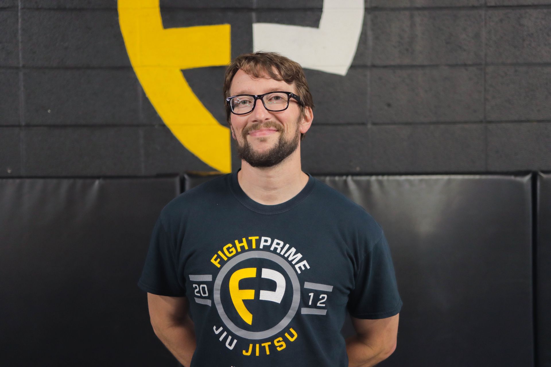 A man wearing glasses and a black shirt is standing in front of a wall.