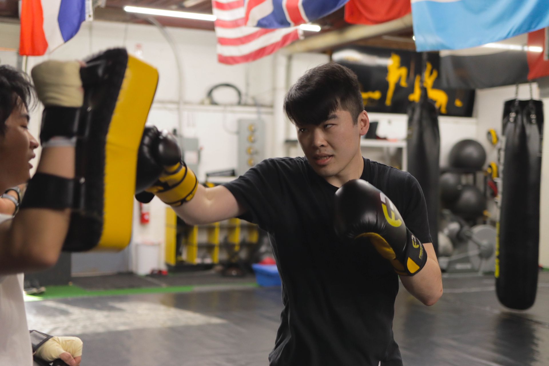 Two men are boxing in a gym with flags in the background.