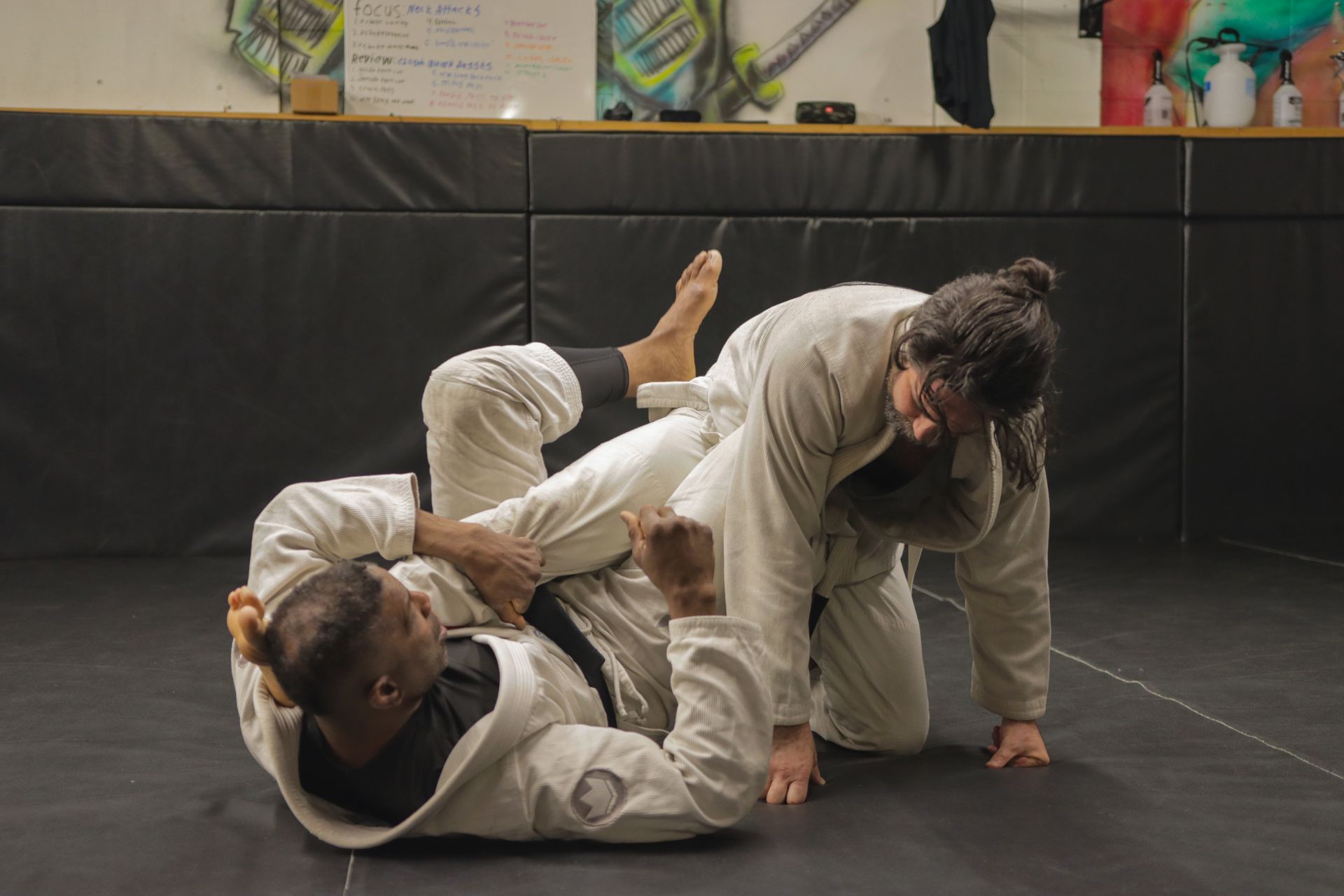 Two people are wrestling on a mat in a gym.