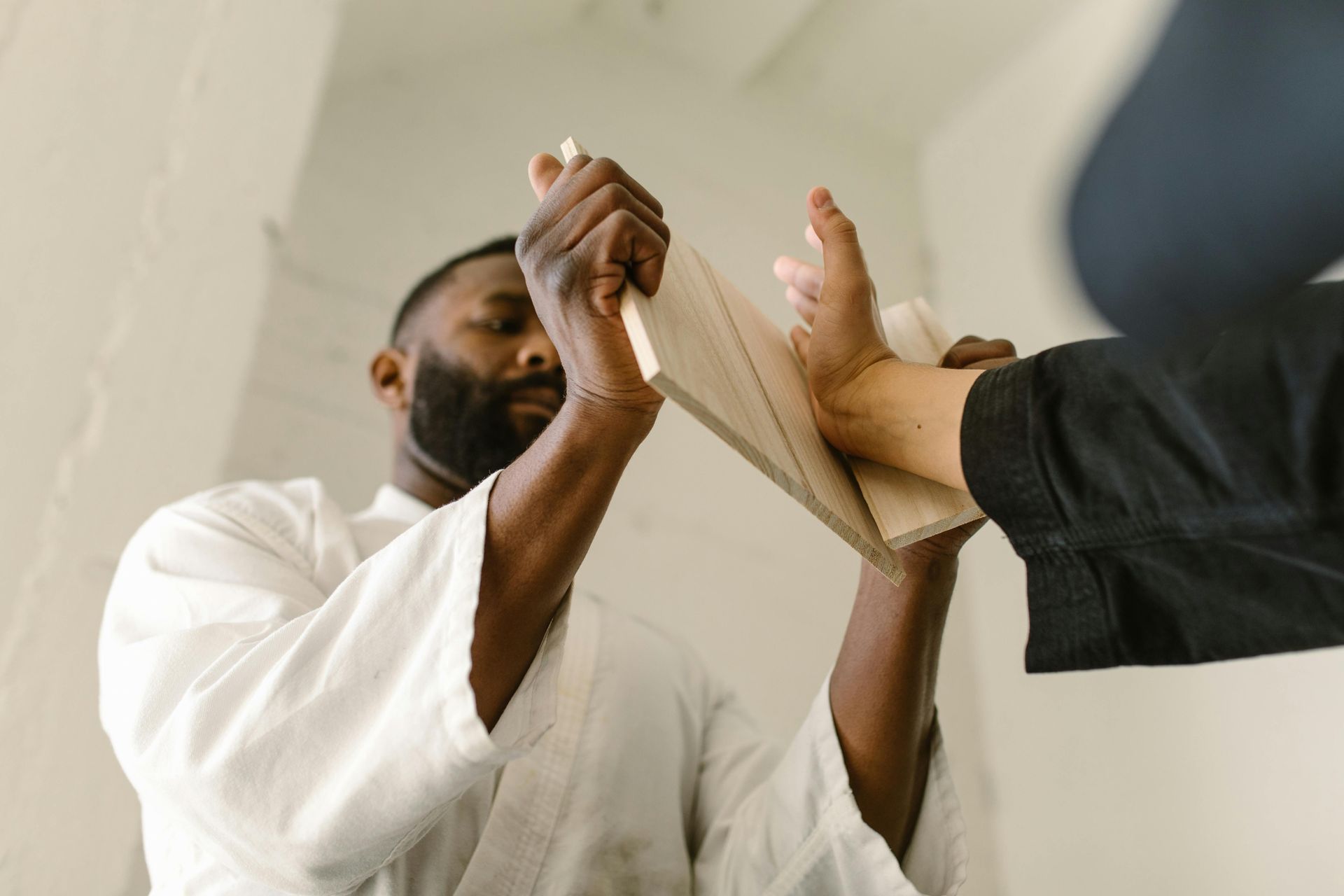 Man in white karate uniform holding a wooden board as a foot kicks through it.