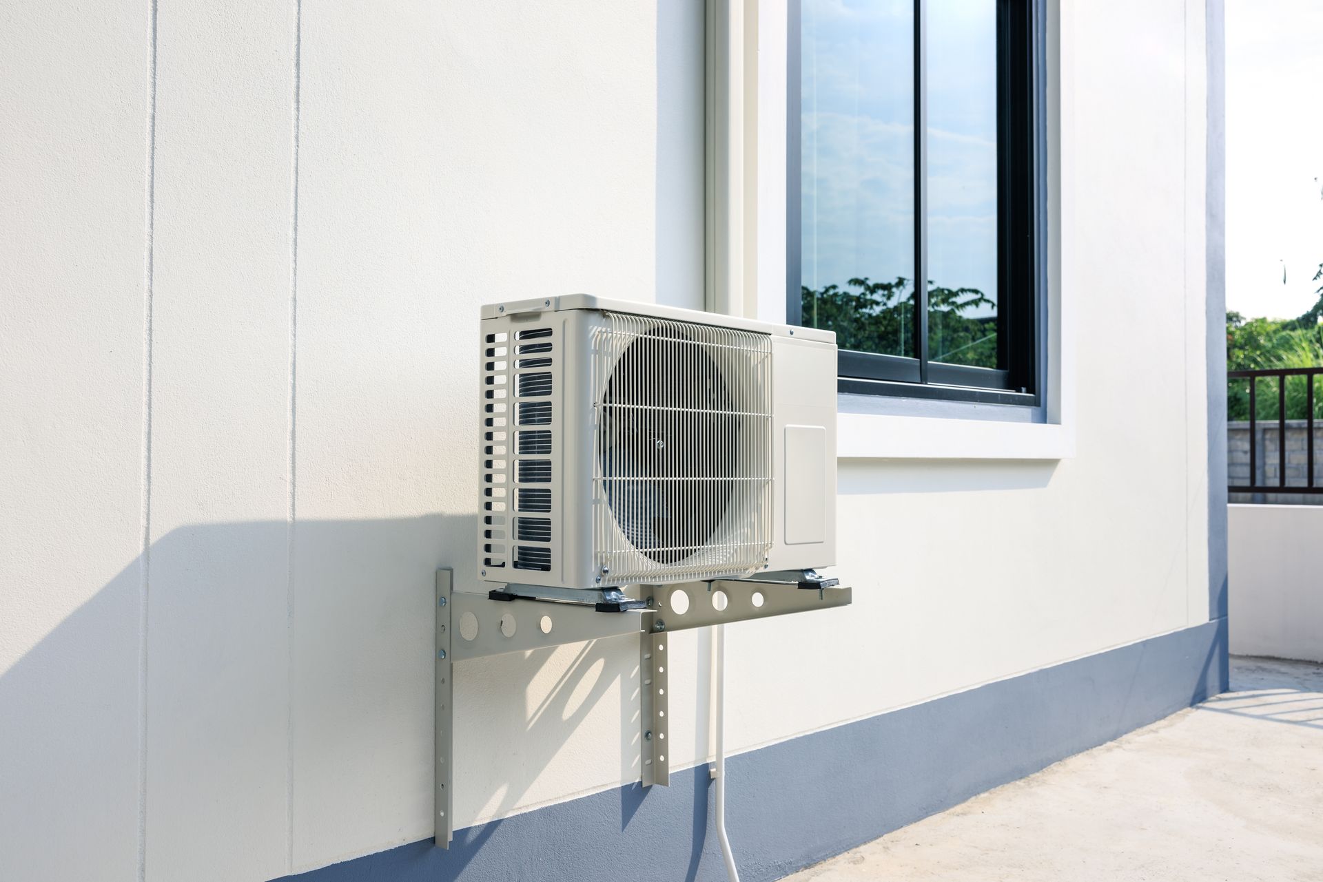 An air conditioner is mounted on the side of a building next to a window.