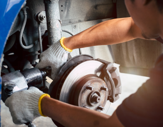 Mechanic using power tool on car brake rotor assembly; wearing gloves, shop setting | Mike's Automotive AC