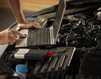 Mechanic using laptop to diagnose a car engine; hands on touchpad, in an engine bay | Mike's Automotive AC