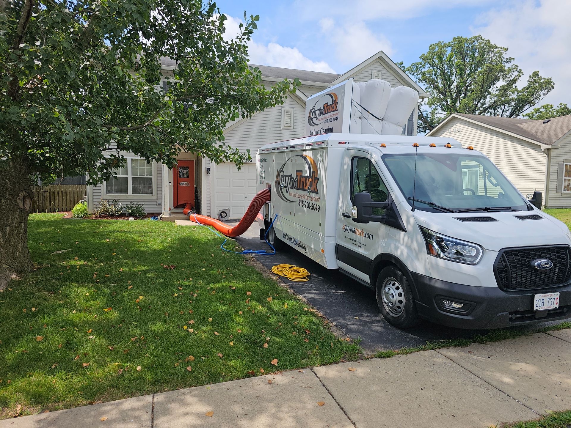 A Guy in a Truck air duct cleaning vehicle parked in driveway with hoses connected to a home.