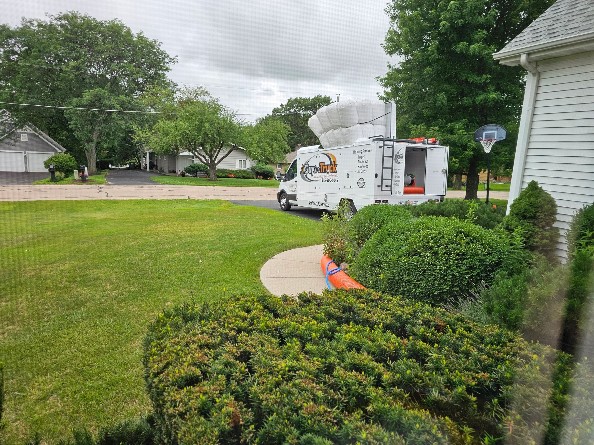 A Guy in a Truck air duct cleaning vehicle parked outside a home with service hoses running inside.