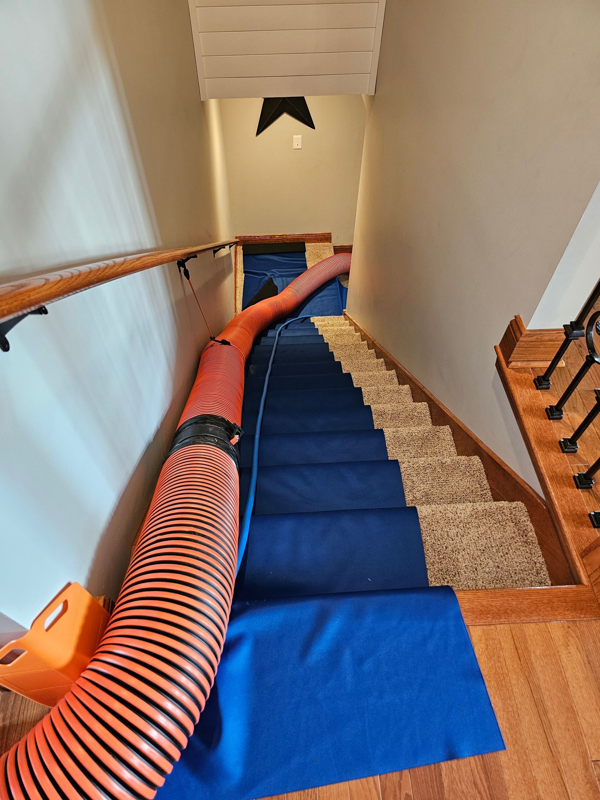 Protective floor covers and duct cleaning hose set up on stairs during residential air duct service.