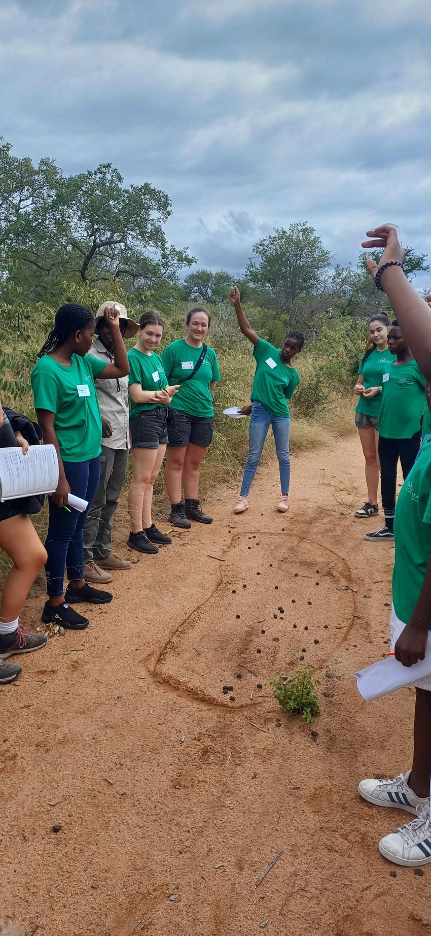 A group of people in green shirts are standing on a dirt road.
