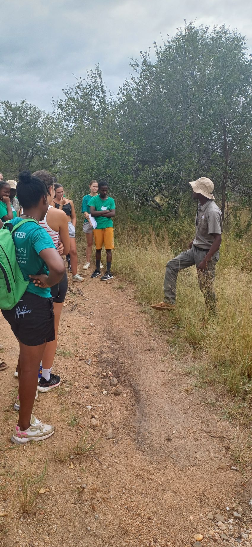 A group of people are standing on a dirt path in the woods.