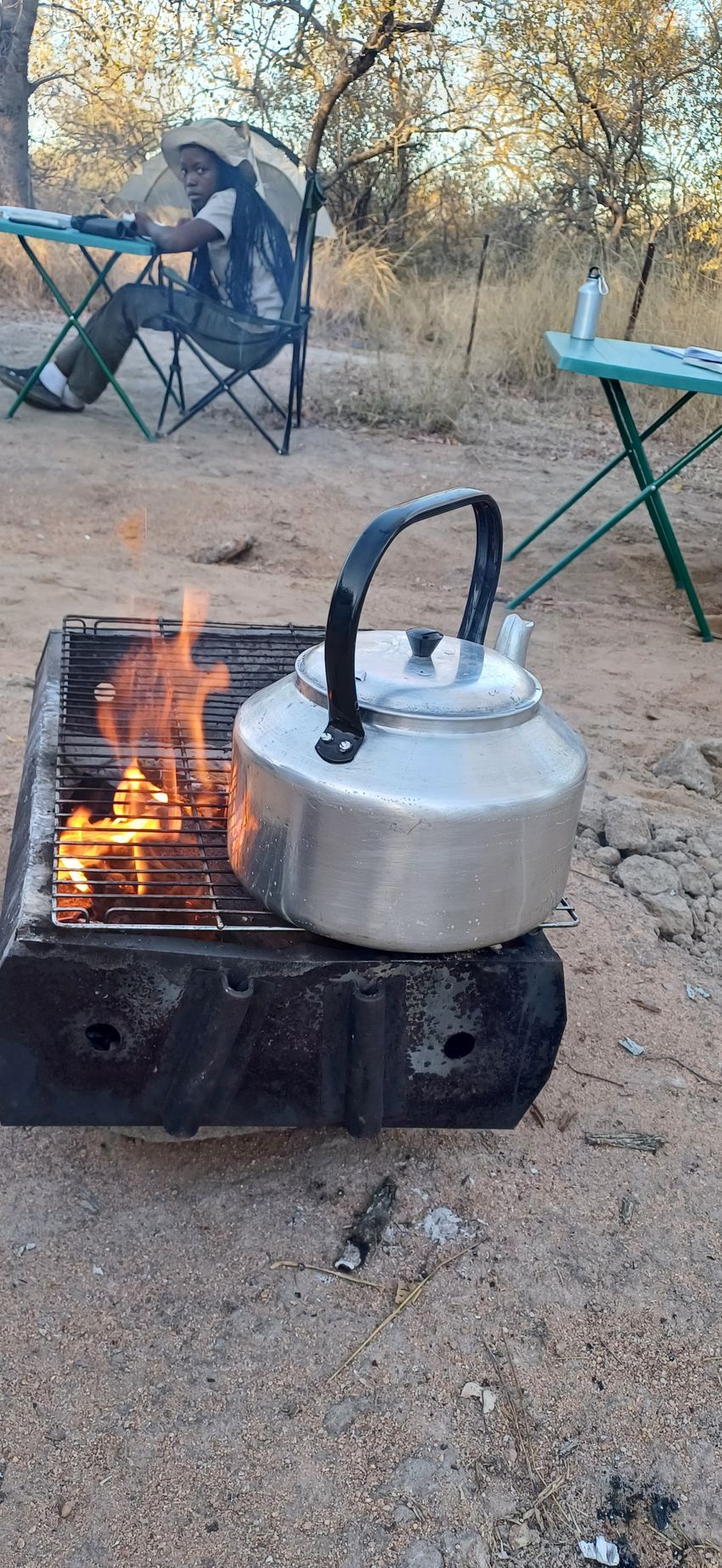 A tea kettle is sitting on top of a fire pit.