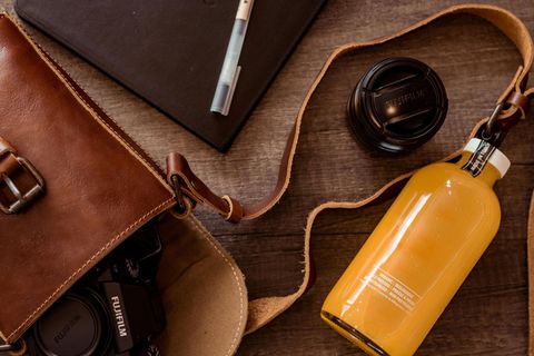 A bottle of orange juice is sitting on a wooden table next to a camera and a notebook.