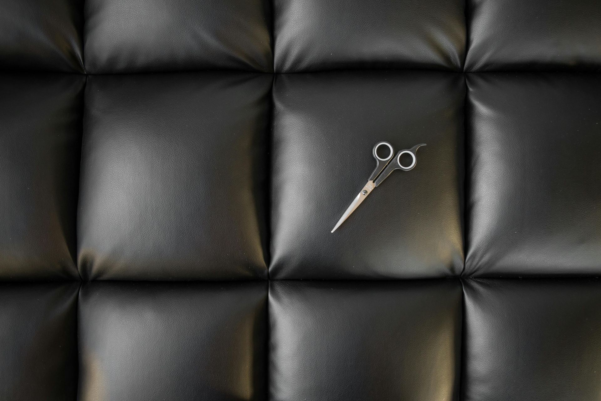 A pair of scissors is sitting on a black leather couch.