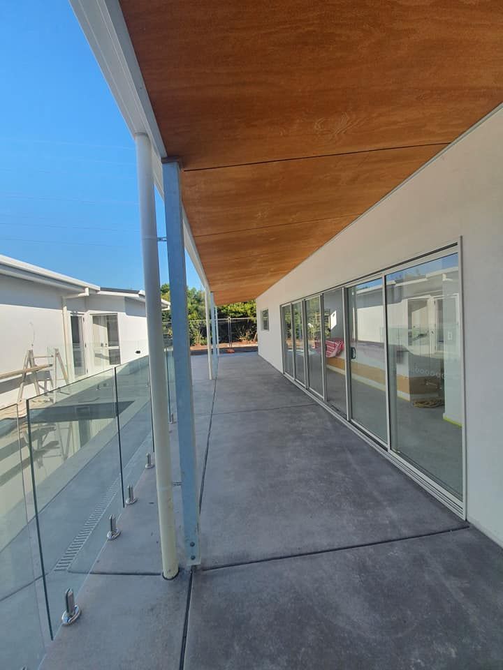 A Long Concrete Walkway With a Glass Railing and a Wooden Ceiling — Jason Walsh Constructions in Lennox Head, NSW