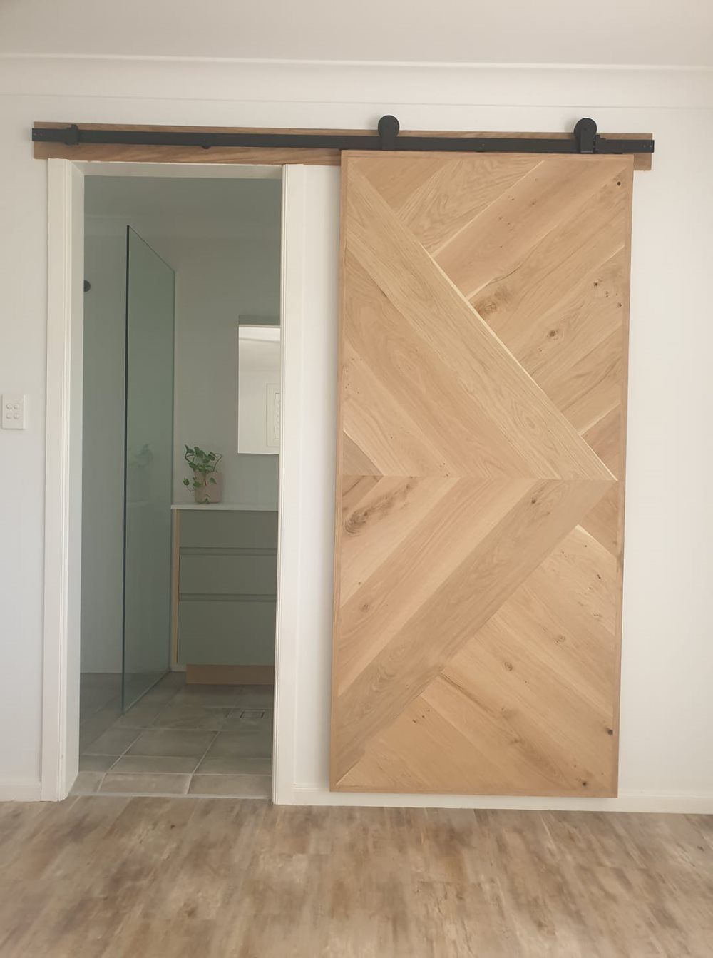 A Wooden Sliding Barn Door is Open to a Bathroom — Jason Walsh Constructions in Lismore, NSW