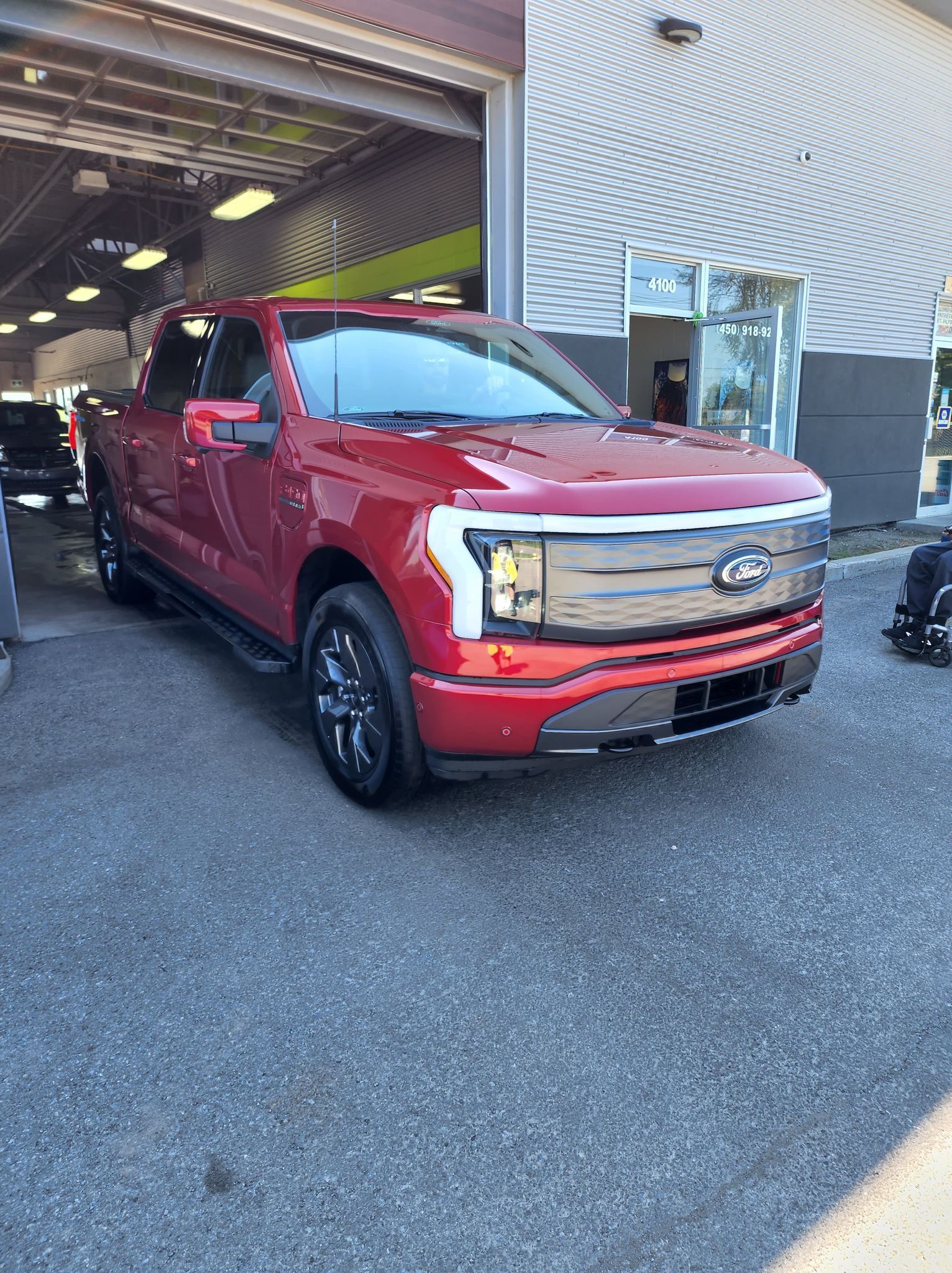 Un camion électrique Ford F150 rouge est garé devant un garage.