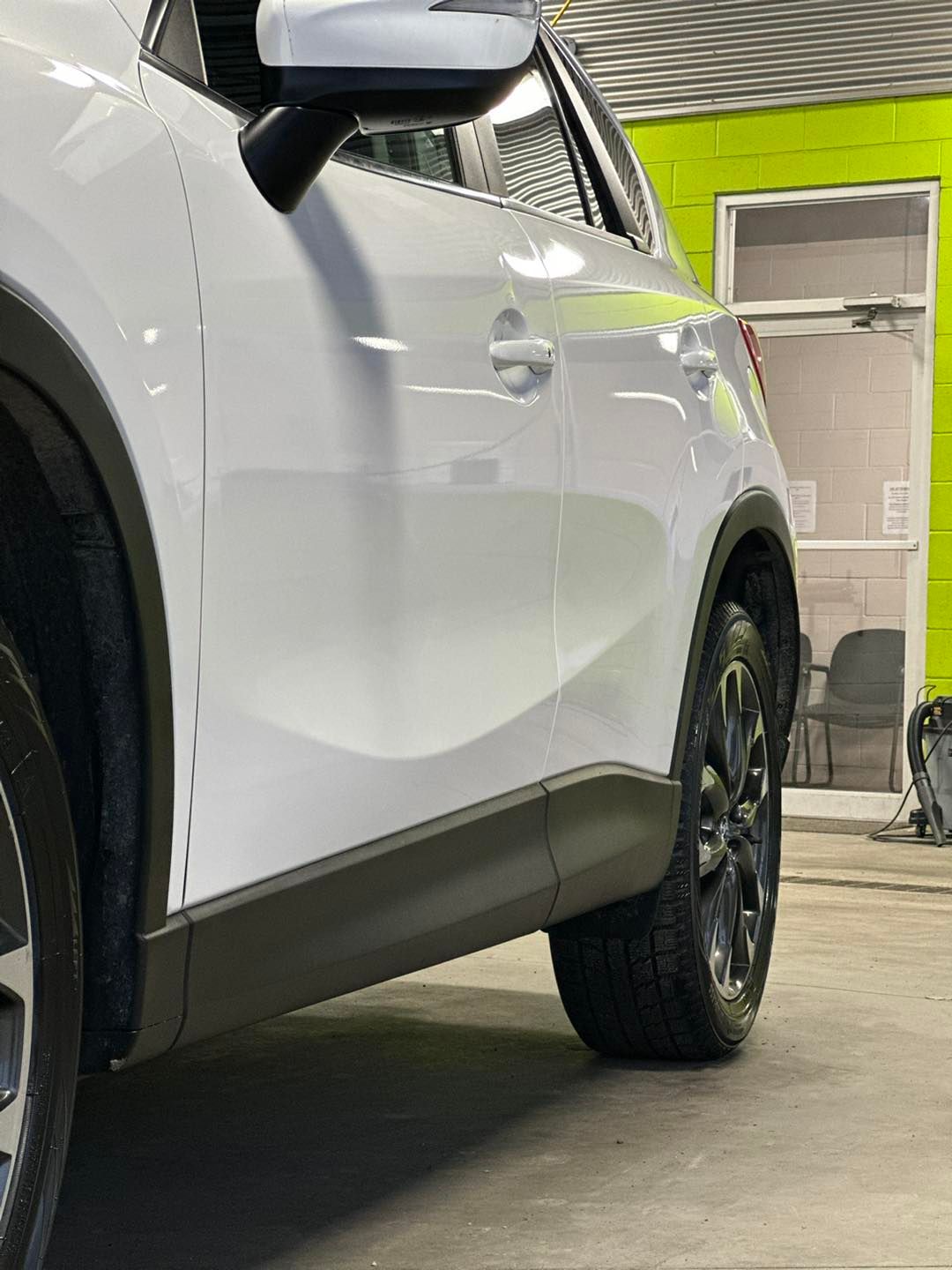 Une voiture blanche est garée dans un garage à côté d'un mur vert.