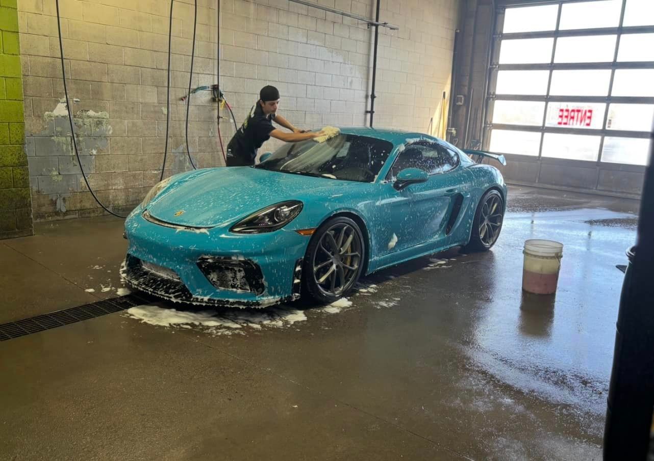 Un homme lave une voiture de sport bleue dans une station de lavage.