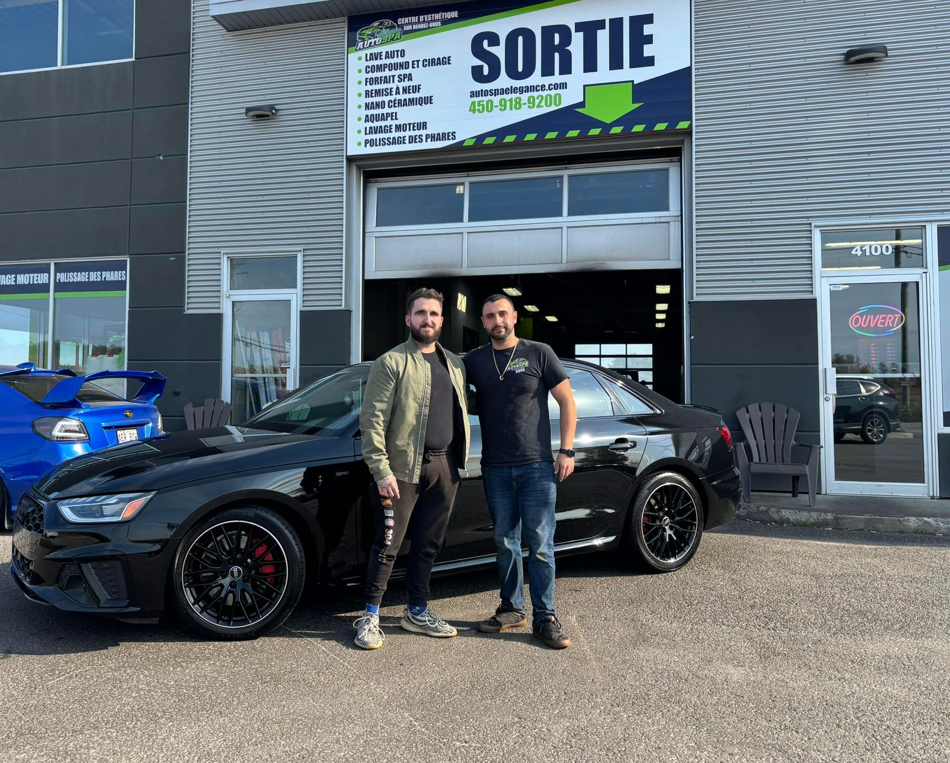 Deux hommes se tiennent à côté d'une voiture noire devant un bâtiment.